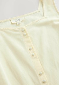 Top sans manches jaune avec un décolleté carré, comportant une rangée de six boutons recouverts de tissu et une texture douce et légère.
