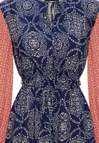 Robe bleu marine avec motifs géométriques blancs, taille smockée et longues manches rouges à motifs. Fabriquée en tissu léger avec un col à nouer.