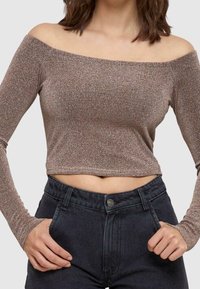 Bronsfärgad off-shoulder långärmad cropped topp i ett texturerat, glänsande material, i kombination med högmidjade mörka denimjeans.