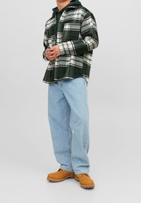 Grünes und weißes karierter Flanellhemd, vorne geknöpft, kombiniert mit hellblauen Jeans und braunen Stiefeln, im entspannten Schnitt.