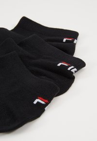 Schwarze Baumwollknöchelsocken mit gerippter Textur, mit weißen und roten Logoakzenten am Bund. In gestapelter Anordnung positioniert.