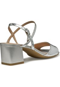 Sandal de tacón bloque plateado con tiras entrecruzadas, parte superior texturizada, punta abierta y un acabado suave y brillante.