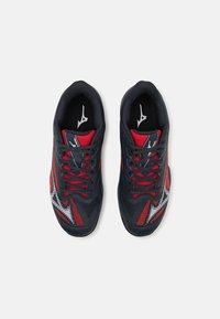 Czarne buty sportowe z czerwonymi akcentami, z teksturowaną cholewką, kontrastującymi wzorami i czarnymi sznurowadłami. Środkowa podeszwa ma smukły design.