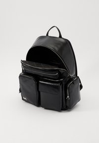 Mochila de cuero negra con la parte superior redondeada, múltiples compartimentos con cremallera, un bolsillo frontal y un logo en la esquina inferior izquierda.