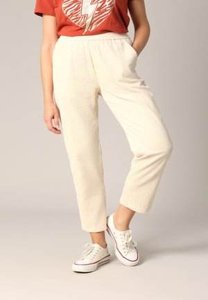 Crèmekleurige corduroy broek met een gestructureerd oppervlak, voorzien van een elastische tailleband en zijzakken, gecombineerd met witte sneakers.