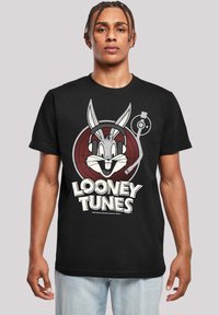 Melnas kokvilnas T-krekls ar grafiku, kurā attēlots Bugs Bunny ar austiņām, centrēts sarkanā mērķī, un balts teksts "LOONEY TUNES" zem tā.