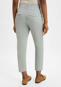 Hellgrüne Hose mit maßgeschneidertem Schnitt, ausgestattet mit zwei Gesäßtaschen mit Knopfverschlüssen und einer glatten Stoffoberfläche.