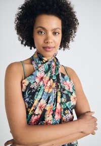 Halter top dengan motif floral yang menampilkan latar belakang hitam dengan bunga berwarna pink, kuning, dan hijau yang cerah, terbuat dari kain yang ringan dan halus.