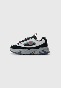 Chunky sneaker with black, white, and gray panels, black laces, and thick Vibram sole, displayed against a plain light gray background.