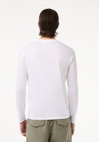 Langærmet hvid t-shirt, lavet af glat stof, med rund halsudskæring og tætsiddende form, parret med olivengrønne shorts.