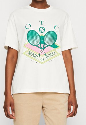 Person trägt ein weißes T-Shirt mit gekreuzten grünen Tennisschlägern, einem Tennisball und dem Text "Marco Polo" in einem geometrischen Design.