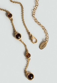 Náhrdelník vo farbe zlata so tromi kruhovými dekoráciami so svetlohnedými a tmavohnedými drahokamami. Obsahuje karabínový uzáver a značkový prívesok.