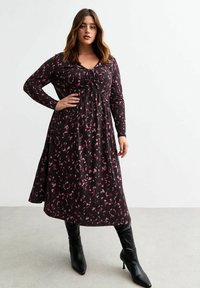 Vestido negro de manga larga con un patrón abstracto en rosa, escote en V, detalles de lazo ajustables y falda acampanada, combinado con botas negras hasta la rodilla.