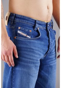 Hellblaue Denim-Jeans im Slim-Fit-Design. Mit Kupferfarbener Hardware, einem gemusterten Taschenfutter und einem geprägten Lederpatch auf der Rückseite.