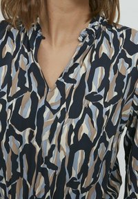 Blouse à manches longues avec un col en V, ornée d'un motif abstrait dans des nuances de bleu, beige et noir, fabriquée en tissu léger.