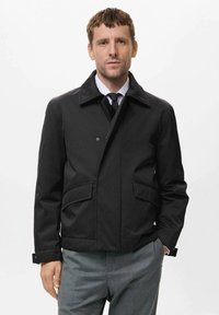 Chaqueta de mezcla de algodón negra con cuello puntiagudo, cierre frontal de botones, dos bolsillos laterales y un diseño ligeramente cropped.