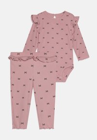 Rózsaszín, bordázott, kétszeletes szett, amely hosszú ujjú bodysuitból áll, fodros vállakkal és hozzá illő nadrágból fodros szegéllyel, feketebow-k díszítésével.