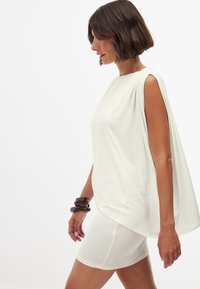 Valge jerserist tunika drapeeritud disainiga, millel on lühikeste varrukate ja sujuva tekstuuriga, koos figuuri rõhutava valge mini-seelikuga.