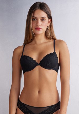 Schwarzer Spitzen-BH mit geformten Cups, verstellbaren Trägern und floralem Muster. Glatte Textur mit gewellten Kanten und zentraler Schleifendetail.