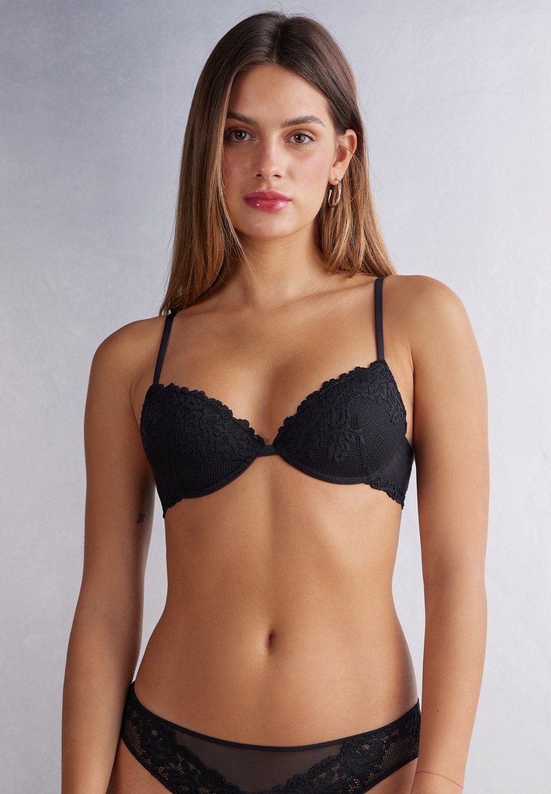 Svart spets-BH med formade kupor, justerbara axelband och blommönster. Mjuk textur med vågiga kanter och en central rosett.