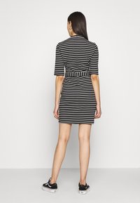 Sukienka w czarno-białe paski z krótkimi rękawami i paskiem w talii, o dopasowanym kroju i długości do kolan, zestawiona z trampkami.