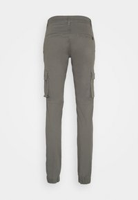 Pantalon cargo gris ajusté avec des poignets élastiques, deux poches passepoilées à l'arrière et des poches à rabat sur les deux cuisses, vu de dos.