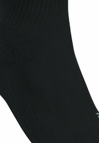 Calzino nero realizzato in un materiale liscio e elastico; presenta un design a coste, una soletta ammortizzata e aree rinforzate per le dita e il tallone.