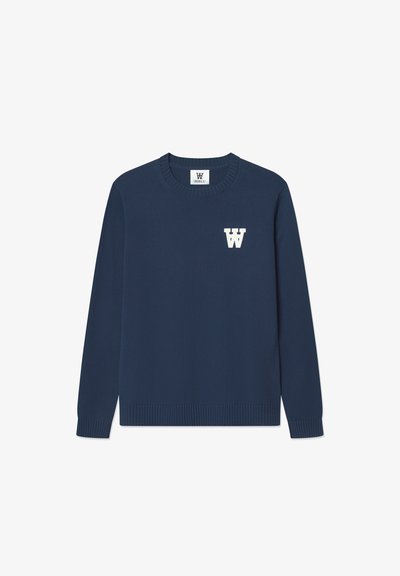 Tummansininen neulepusero, jossa on pyörökaulus, ribattu helma ja pitkät hihat. Vasemman rinnan kohdalla on valkoinen "W"-logo.