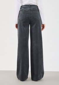 Pantalons à jambe large en velours côtelé gris foncé, avec une taille haute, deux poches arrière, une texture visible et une coupe droite des hanches jusqu'en bas.