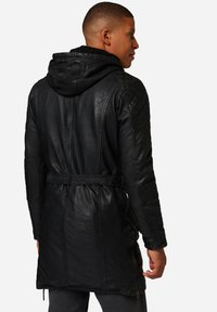 Schwarzer Lederumhang mit Kapuze, gesteppte Schulterpaneele, taillierter Bund und seitlichen Reißverschlüssen, die eine glatte Textur und eine maßgeschneiderte Passform zeigen.