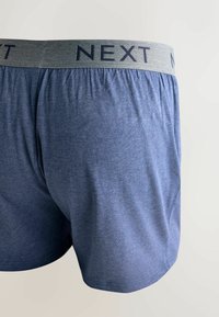 Modré bavlnené boxerky s elastickým sivým pásom, na ktorom je tmavými písmenami vytlačené "NEXT". Hladká textúra, voľný strih a bez viditeľných vzorov.
