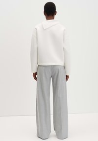 Maglione bianco oversize con colletto a coste, abbinato a pantaloni larghi grigi chiari in un tessuto morbido, visto da dietro.