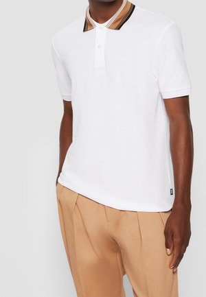 Polo blanc avec un col rayé brun foncé et beige, doté d'une patte de boutonnage à trois boutons et d'un logo discret sur la poitrine.