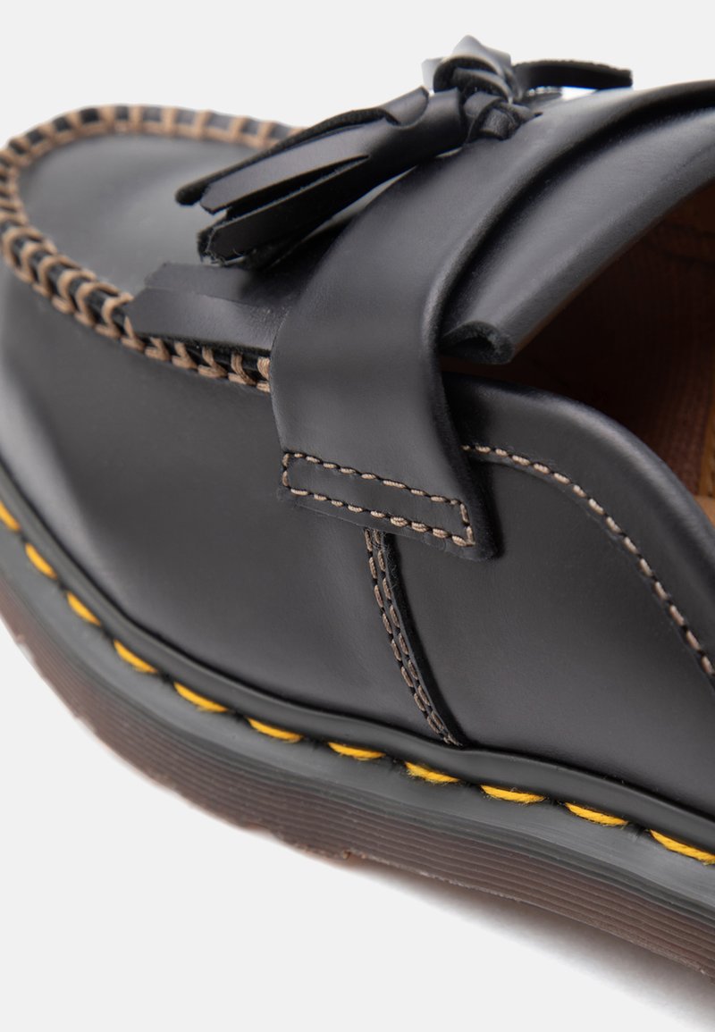 Schwarzer Lederloafer mit Quasten, kontrastierenden Nähten und einer dicken Sohle mit gelben Nahtdetails.