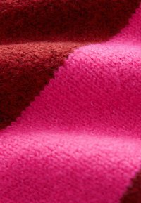 Textielstof met een rood en levendig roze kleurenpalet, met een zachte, gestructureerde oppervlakte en uitgesproken, verhoogde patronen.