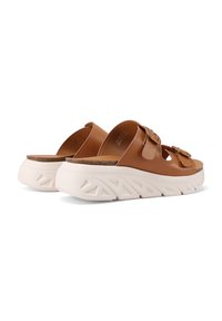 Sandali in pelle marrone slip-on con due fibbie, plantare in sughero e suola piatta bianca spessa con un motivo geometrico testurizzato.