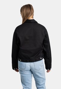 Chaqueta de mezclilla negra con cuello, mangas largas y cierres de botón a presión. Presenta una textura suave y un diseño ligeramente corto.