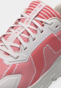 Detailný záber na ružovobielu športovú obuv s bielymi šnúrkami a pásikavým jazykom, ktorý má textúrovanú sieťovinu a podporné prekrytia.