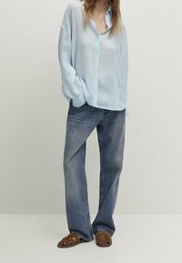 Ljusblå skjorta med knappar och långa ärmar, i kombination med blå raka jeans och bruna sandaler med remmar. Enkelt mönster och avslappnad passform.