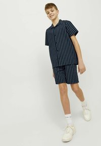 Chemise à rayures marines à manches courtes et shorts assortis en tissu léger. Boutons blancs et coupe décontractée. Le modèle porte des baskets blanches.