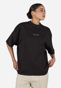 Black oversized t-shirt with a high neckline and short sleeves, featuring a white "PEGADOR" logo on the front. Smooth cotton fabric.