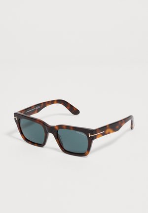 Lunettes de soleil rectangulaires écaille avec verres foncés et subtils accents dorés sur les branches, marquées Tom Ford sur le verre.