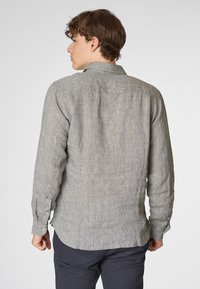 Camicia grigia in lino a maniche lunghe con polsini a bottone, vestibilità rilassata, colletto sul retro e texture sottile, indossata con pantaloni scuri.