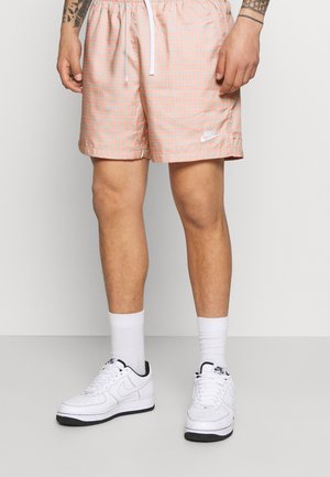Roze geruite zwemshorts met een elastische tailleband en een witte trekkoord. Gecombineerd met witte sneakers en witte kousen.