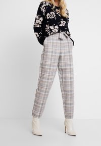 Svart tröja med blommönster i stickad design, bärs över ljusgrå rutiga byxor med knytmidja, i kombination med beiga stiletto ankle boots.