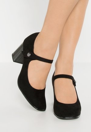 Talons Mary Jane en daim noir avec un bout rond, une sangle ajustable et un talon bloc moyen comportant un accent circulaire.