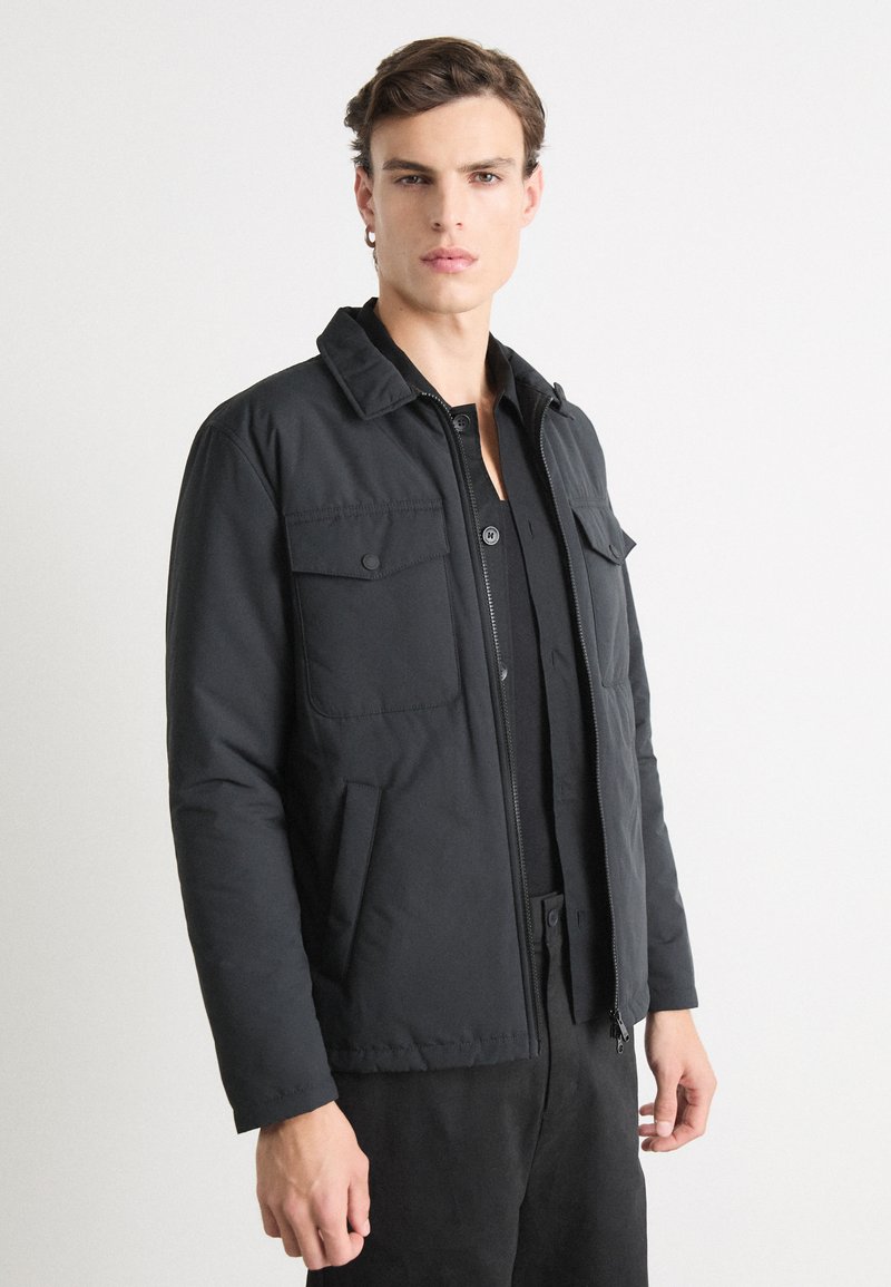 Schwarze Zip-Jacke aus strukturiertem Stoff, mit zwei Fronttaschen und einem spitzen Kragen. Lange Ärmel mit lockerer Passform.