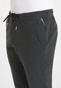 Donkergrijze sweatpants met een trekkoord in de taille, zijzakken, een achterzak en een klein merklabel op de rand van de rechterzak.