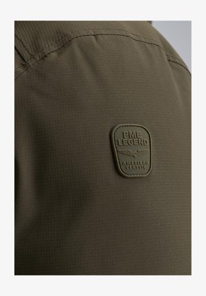 Olivgrüner Stoff mit einem strukturierten Rautenmuster, versehen mit einem rechteckigen Gummipatch mit geprägt: "PME LEGEND AMERICAN CLASSIC."