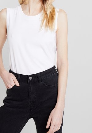 White sleeveless cotton top paired with high-waisted black denim jeans. Jeans have a metal button and front pockets.